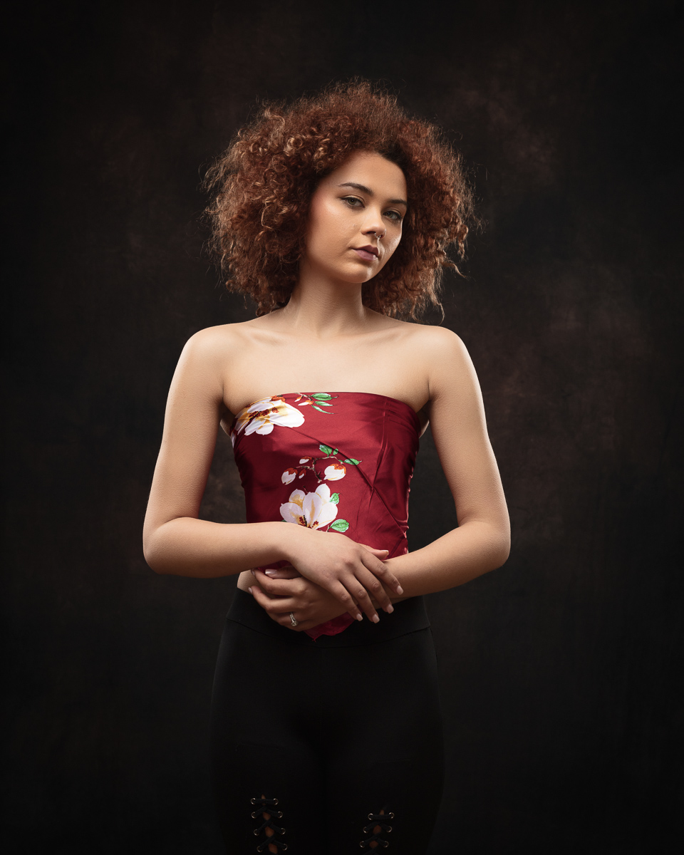 Woman in floral strapless top, dark background.