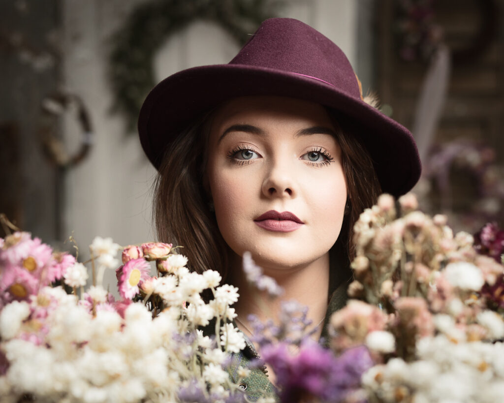 Woman in hat surrounded by colourful flowers.