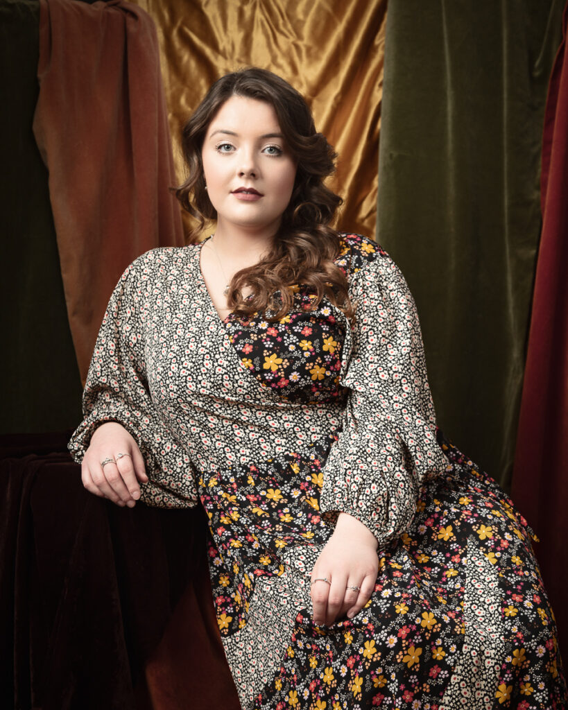 Woman in floral dress with coloured velvet backdrop.