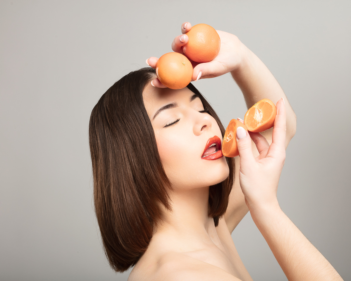 Woman posing with oranges against neutral background.