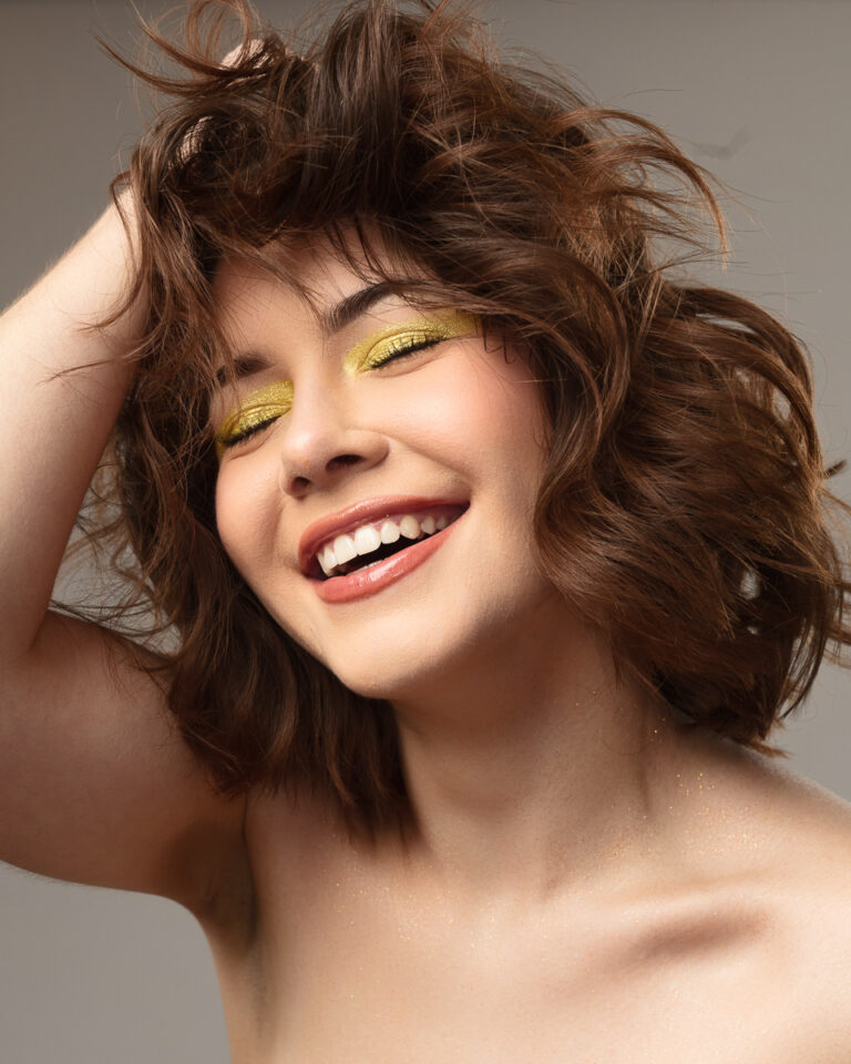 Woman smiling with closed eyes and yellow eyeshadow.
