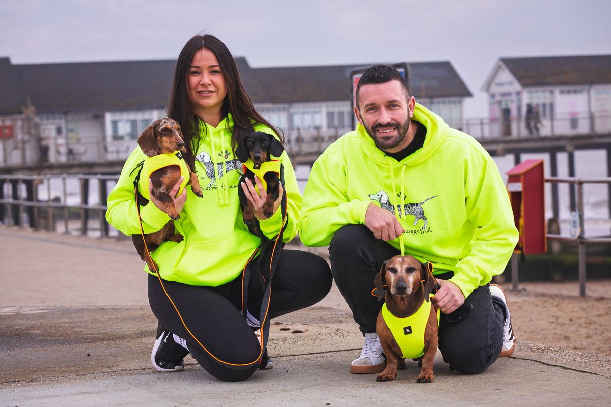 Two people in high-visibility jackets with their dachshunds on the promenade at Southwold