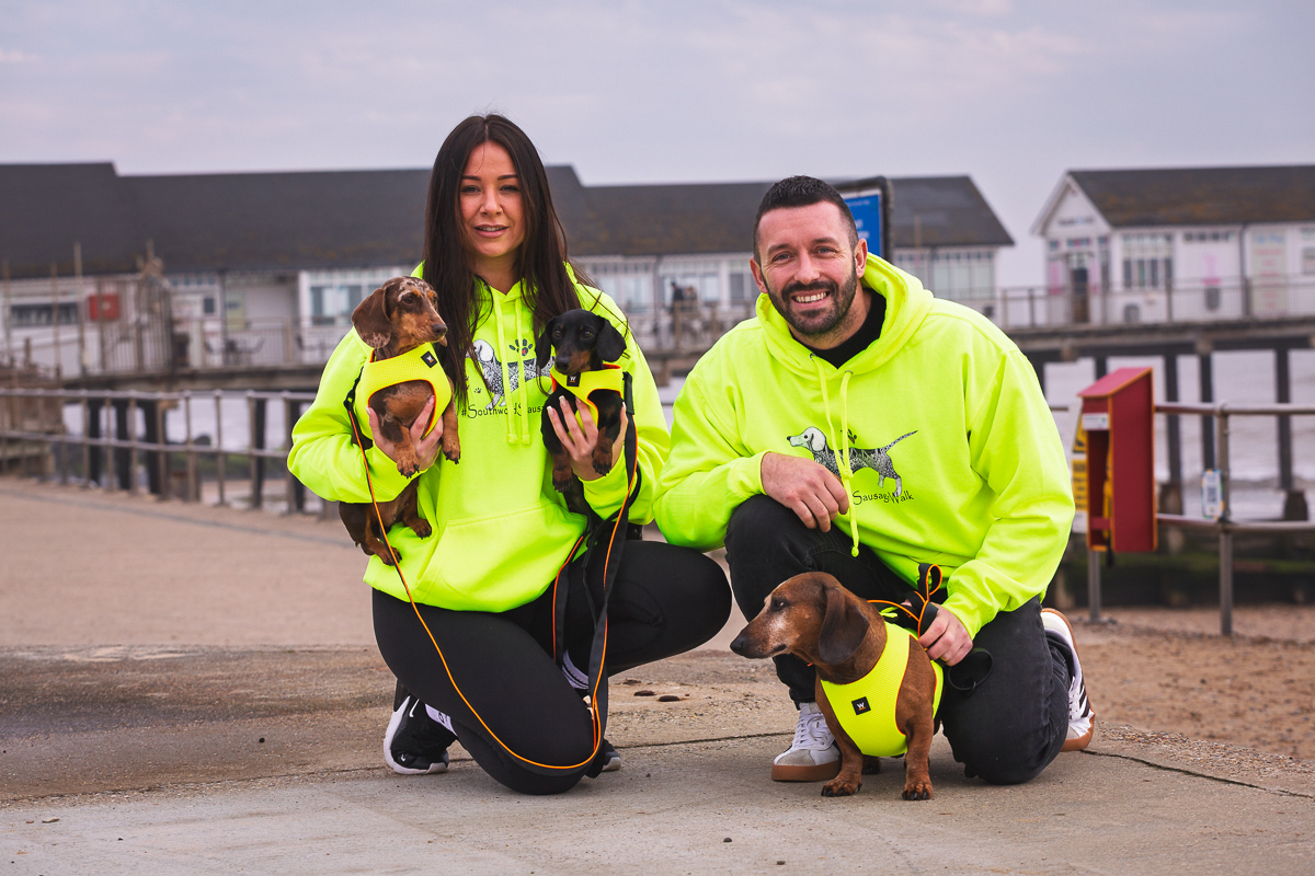 Couple with dachshunds on seaside walk in bright hoodies.