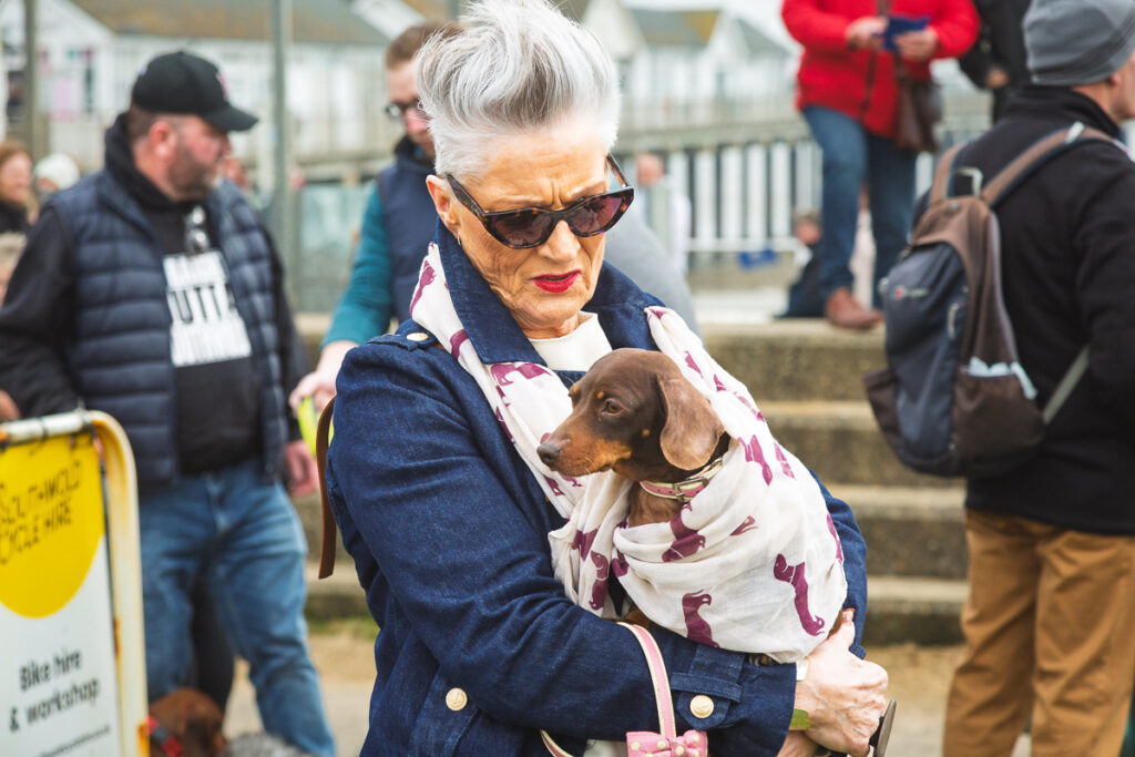 Woman holding dachshund wrapped in scarf outdoors.