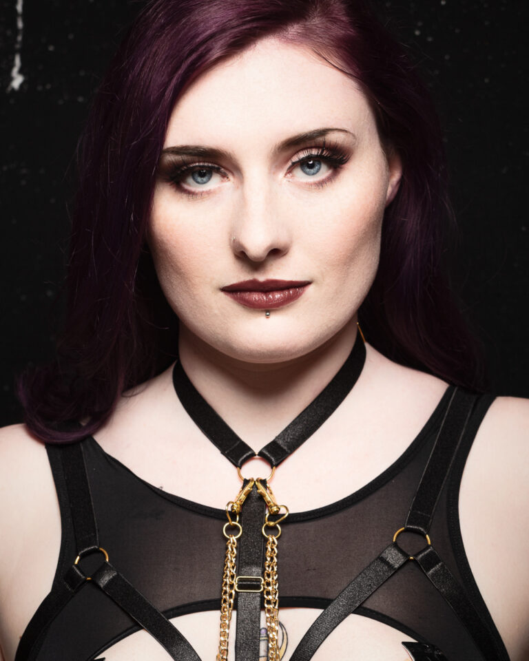 Person with purple hair, gold and black necklace.