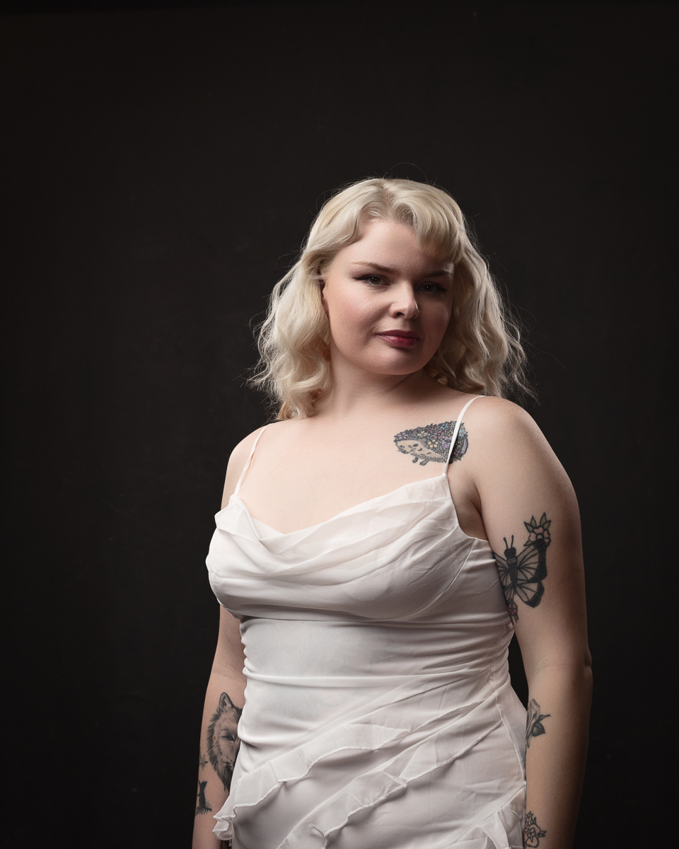 Blonde woman with tattoos wearing a white dress.