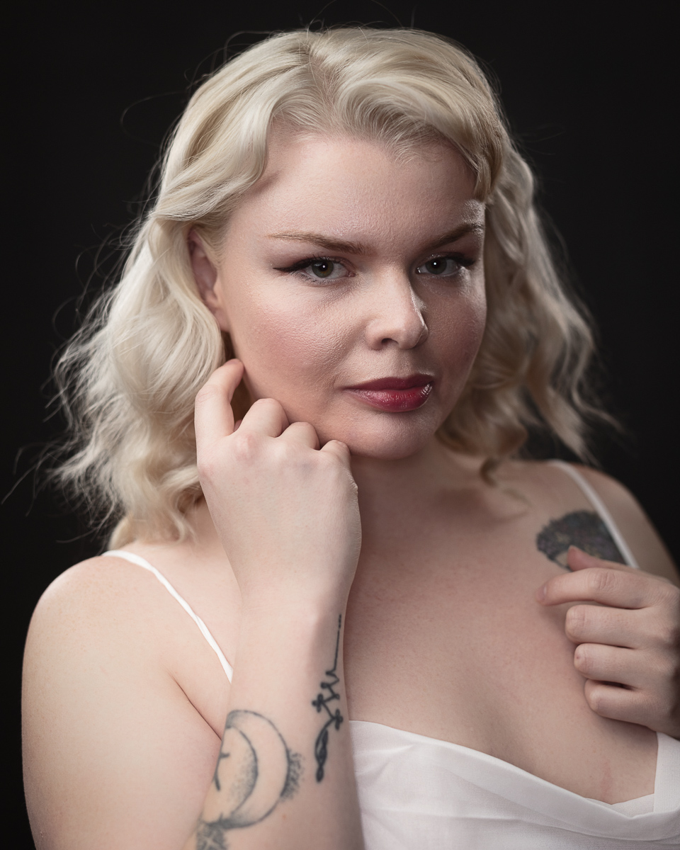 Blonde woman with tattoos against dark background.