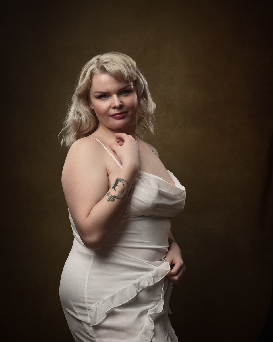 Woman in white dress with tattoo posing elegantly.