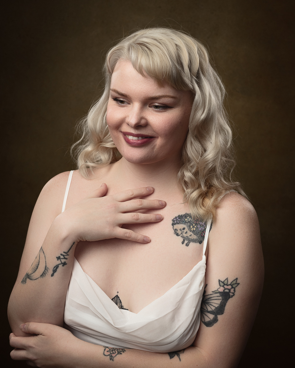 Smiling woman with tattoos, hand on chest.