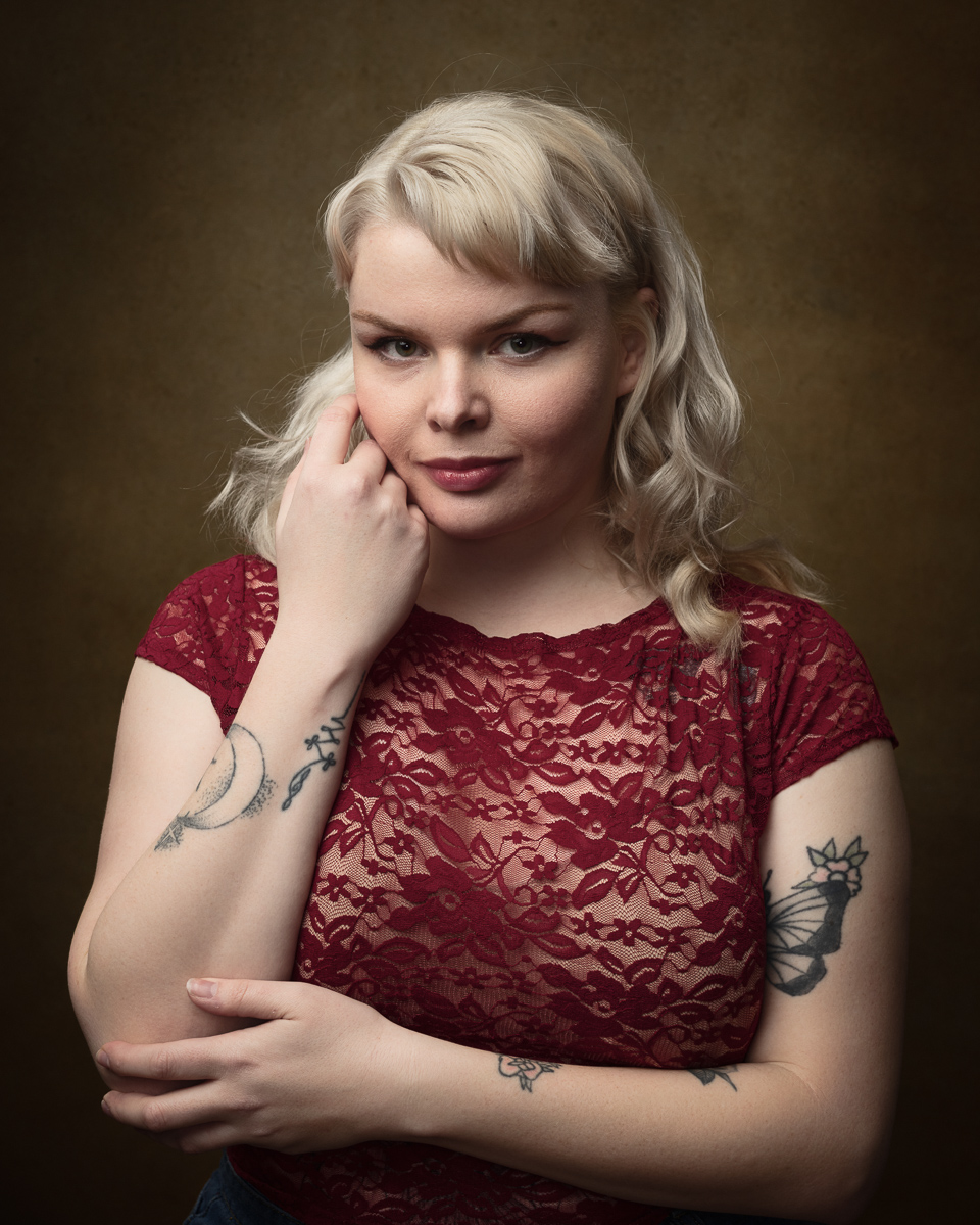 Woman with tattoos in red lace top, studio portrait.