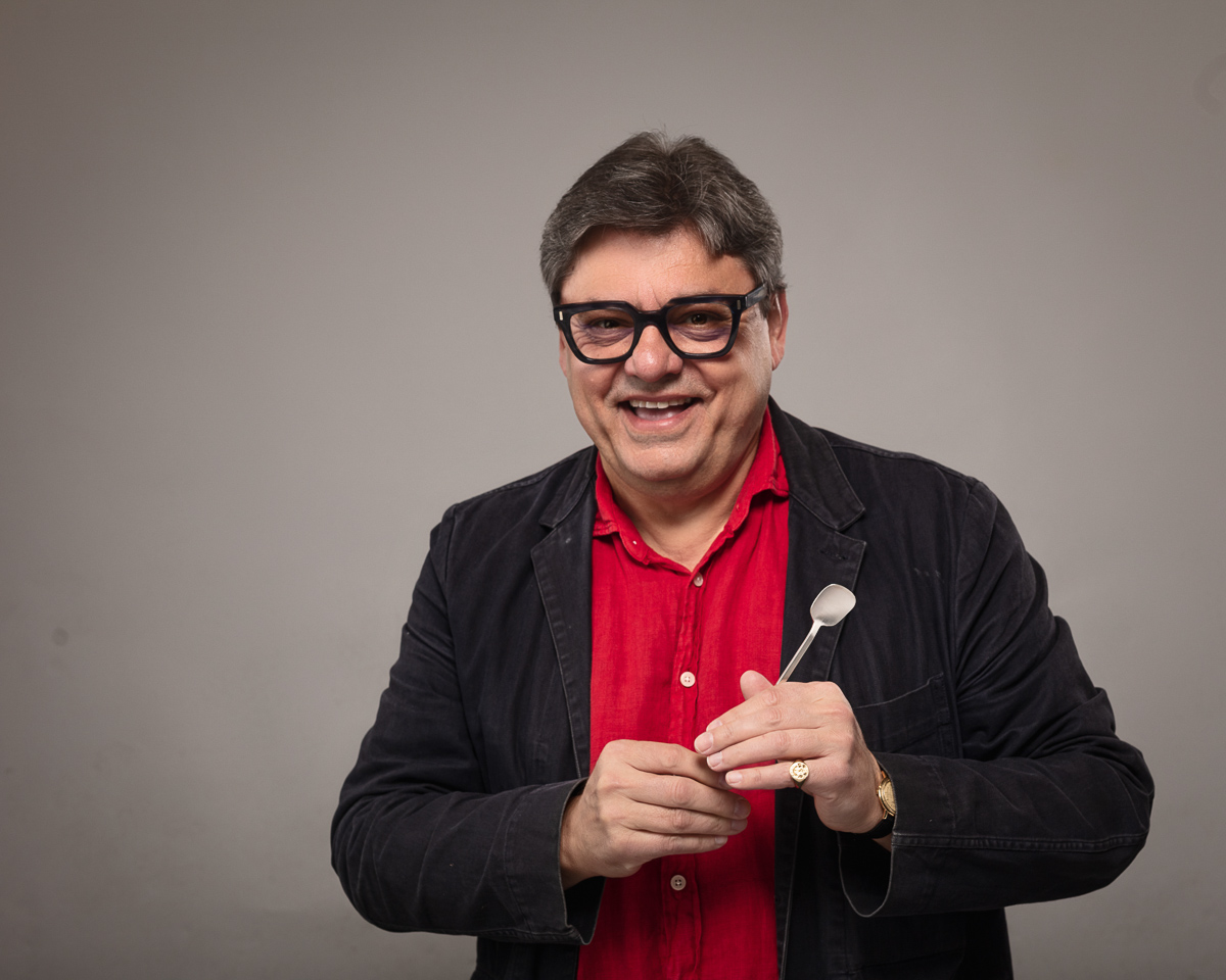 Smiling man holding spoon, wearing glasses and red shirt.