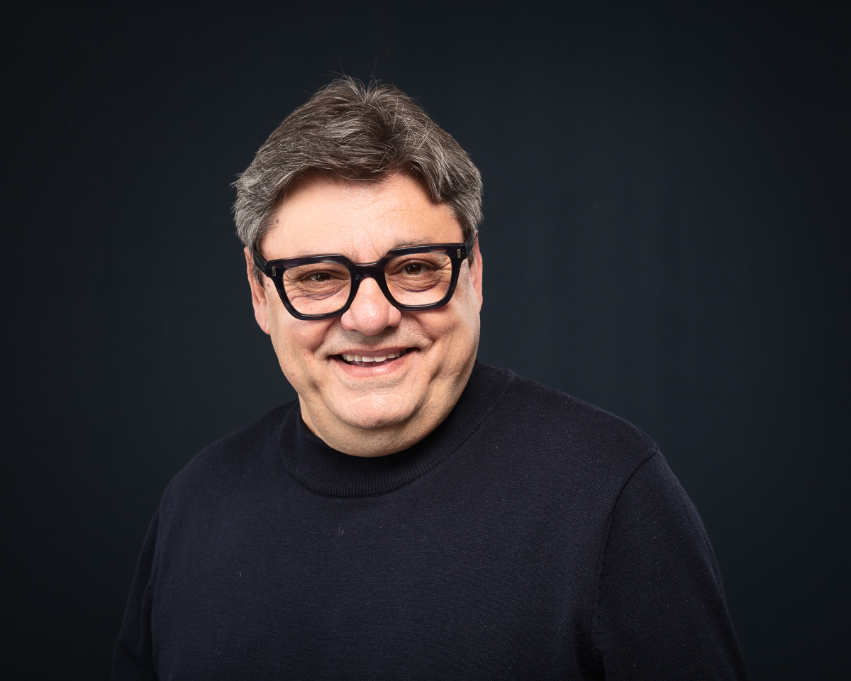 Smiling person with glasses against dark background.