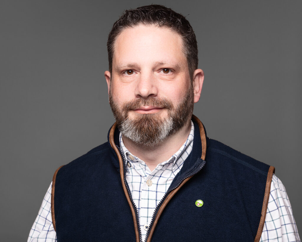 Man with beard and checked shirt smiling.