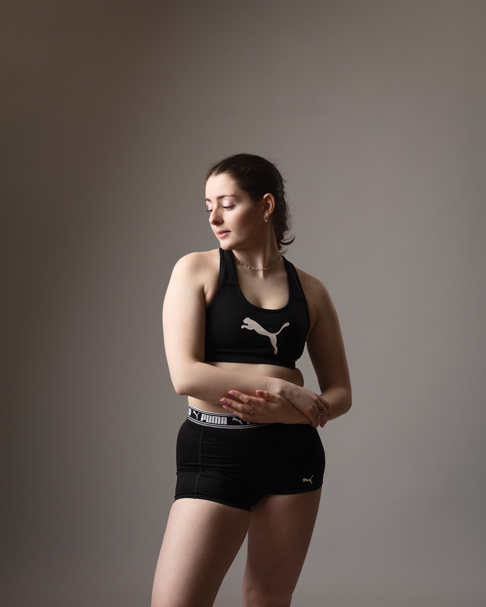 Woman in black sports attire posing, grey background.