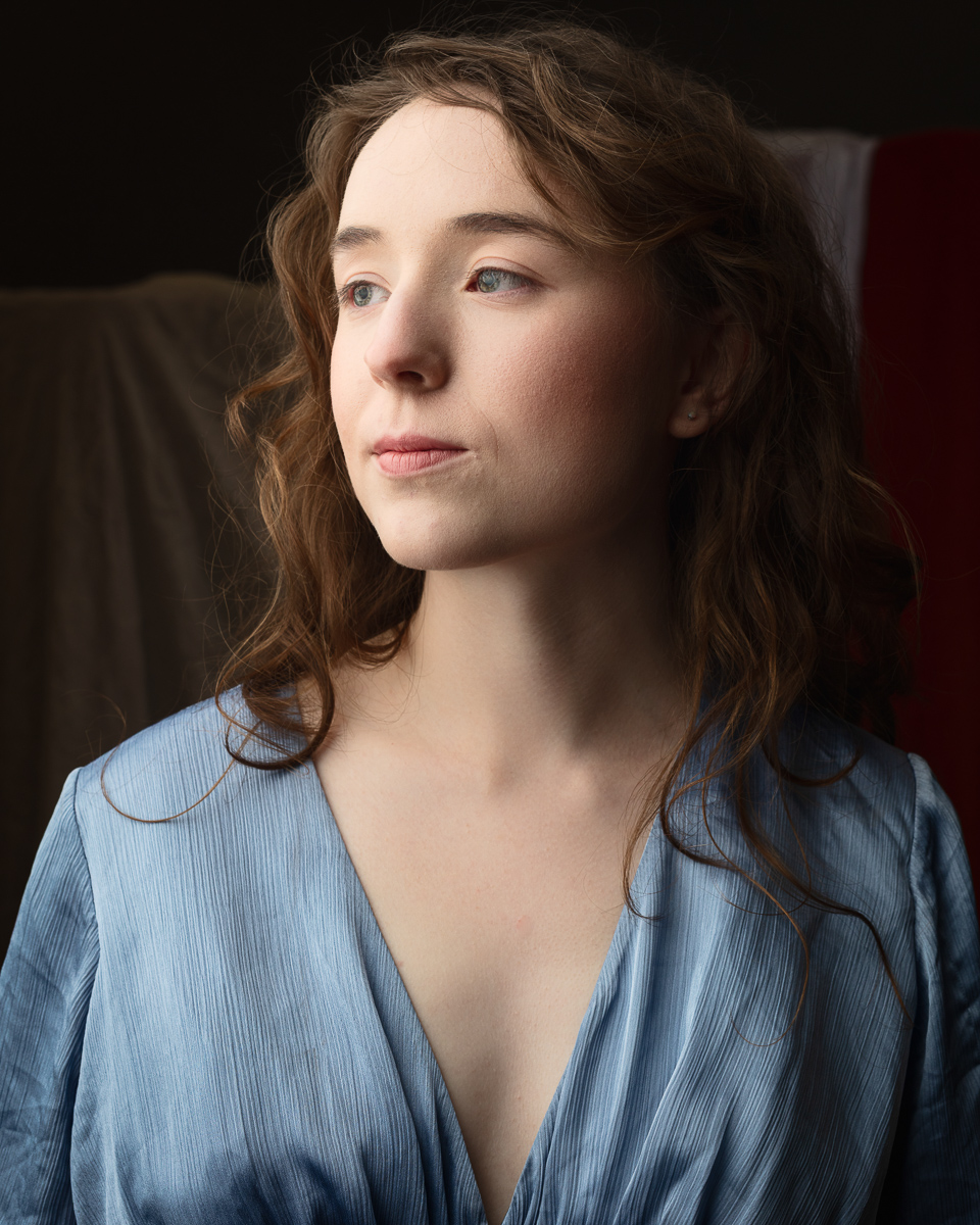 Woman in blue dress gazing thoughtfully sideways.