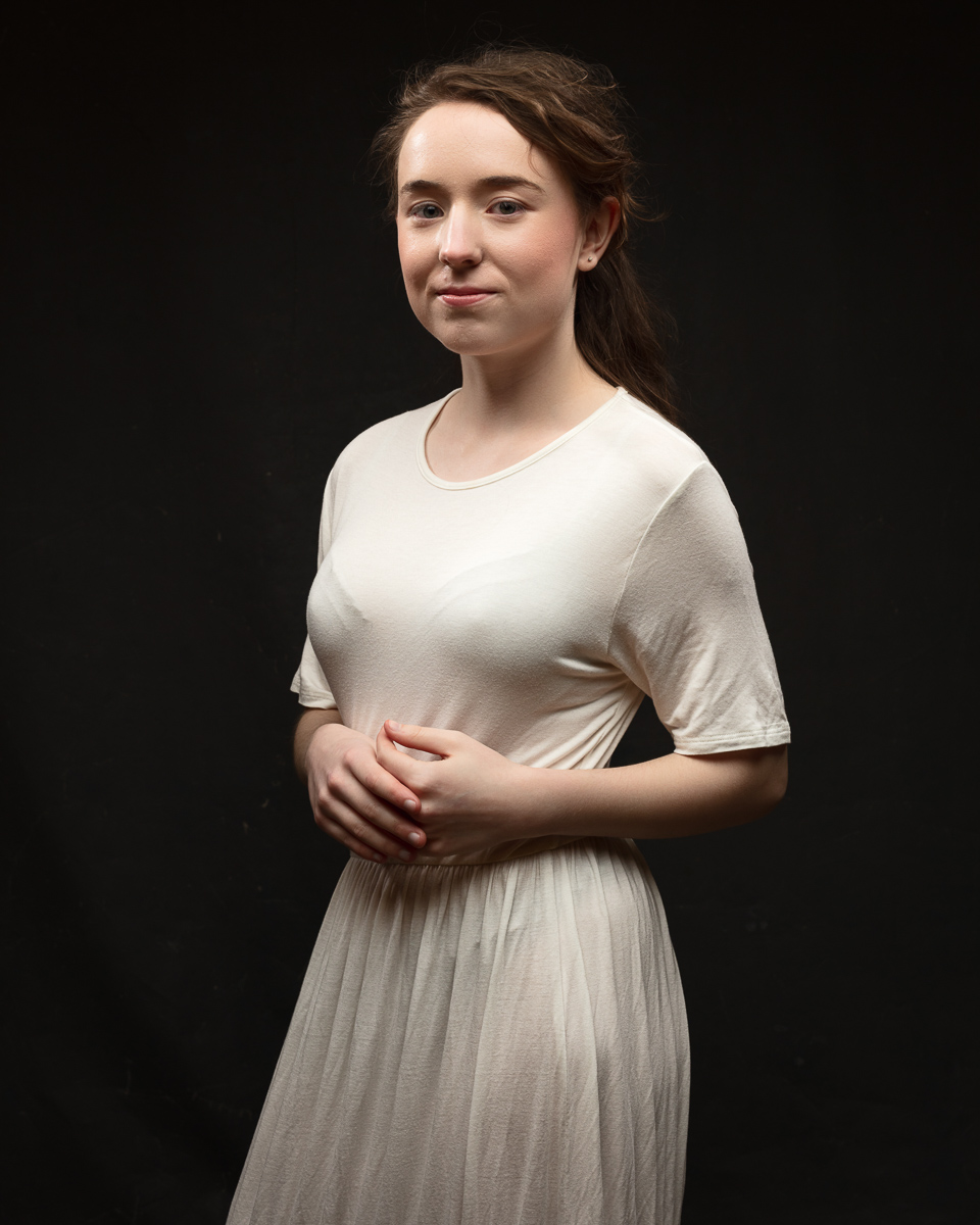 Woman in white dress posing against dark background.