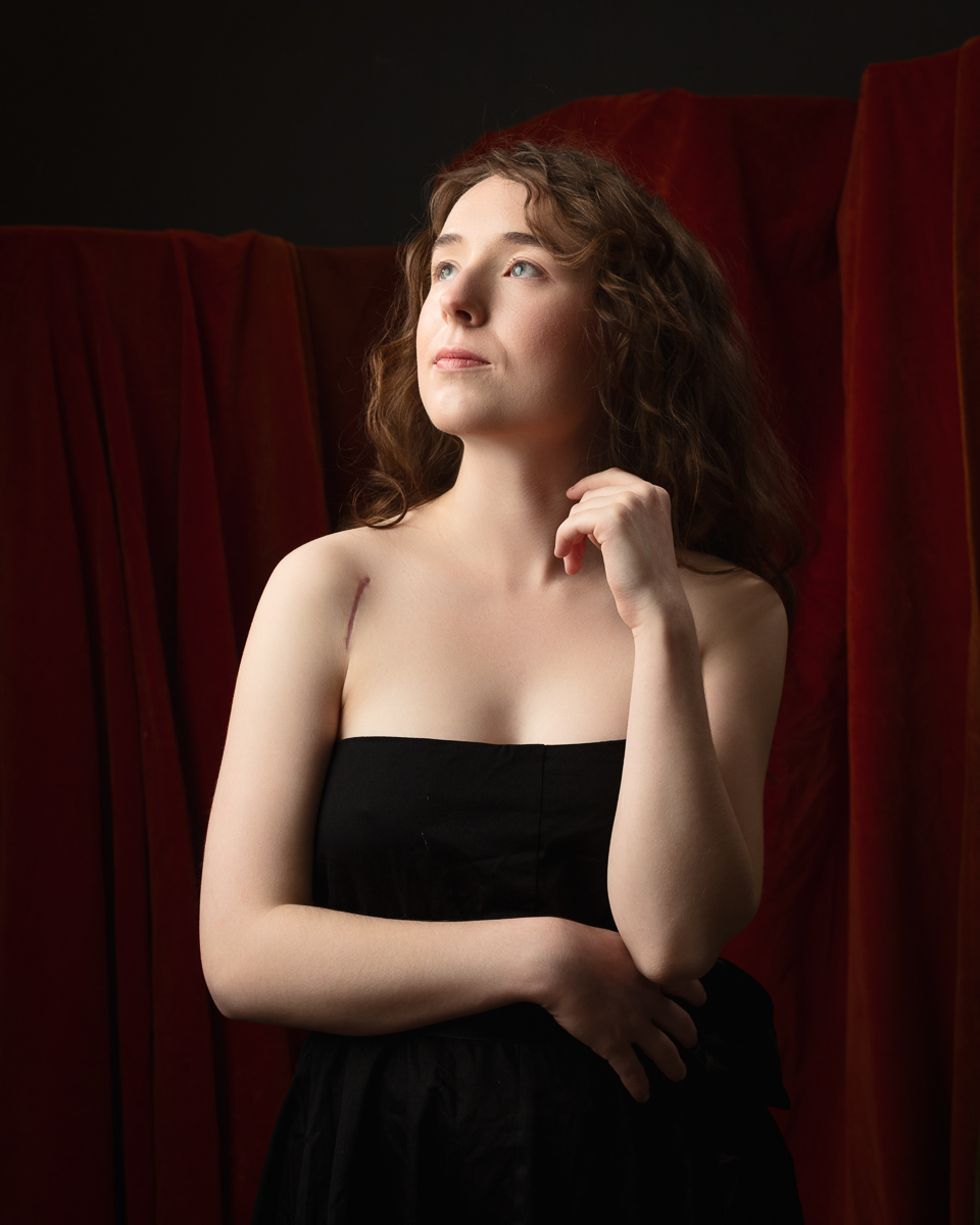 Thoughtful woman in black dress with red curtains.
