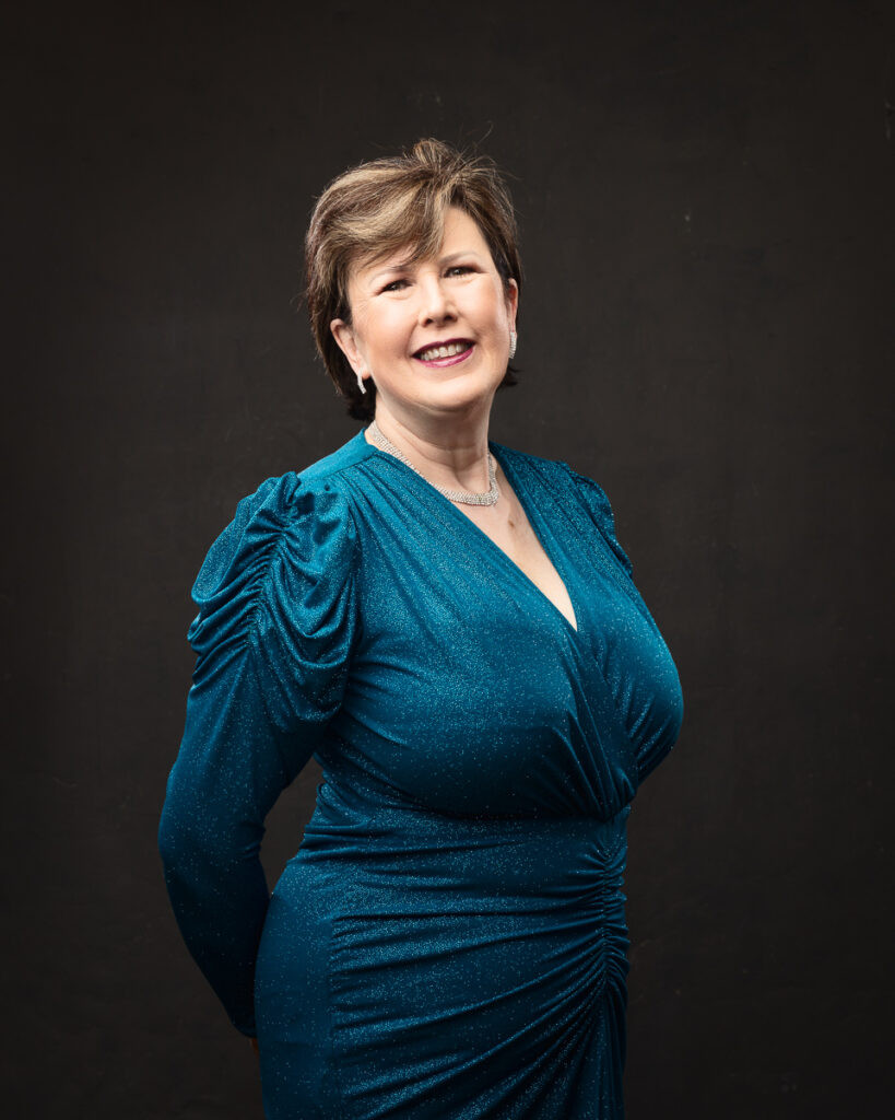 Smiling woman in elegant blue dress against dark background.