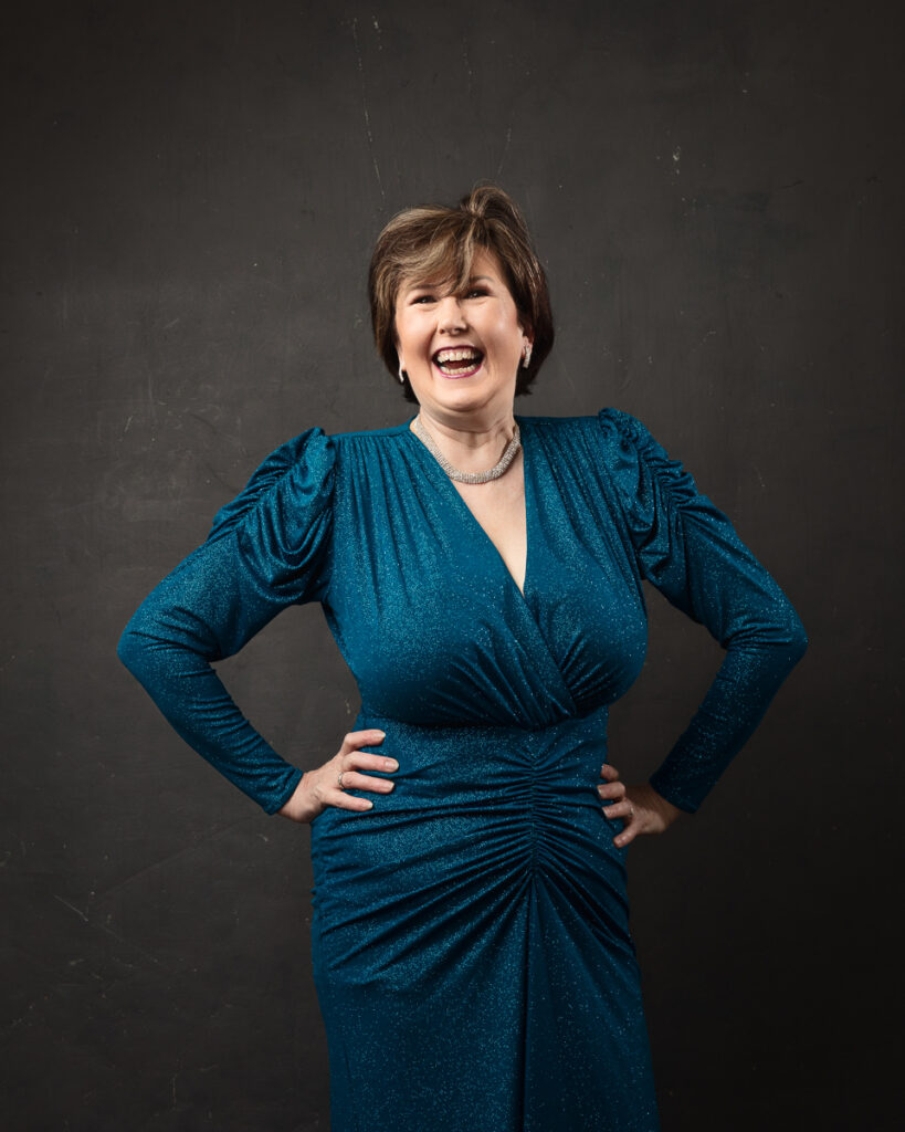 Smiling woman in sparkling blue dress against dark background.