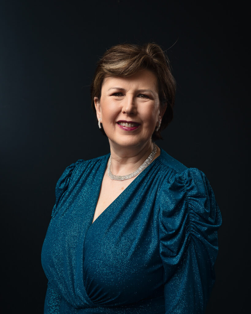 Smiling woman in blue dress, dark background.