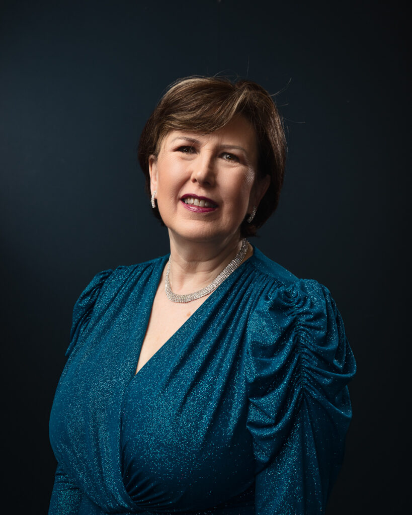 Person in blue dress and necklace, smiling.