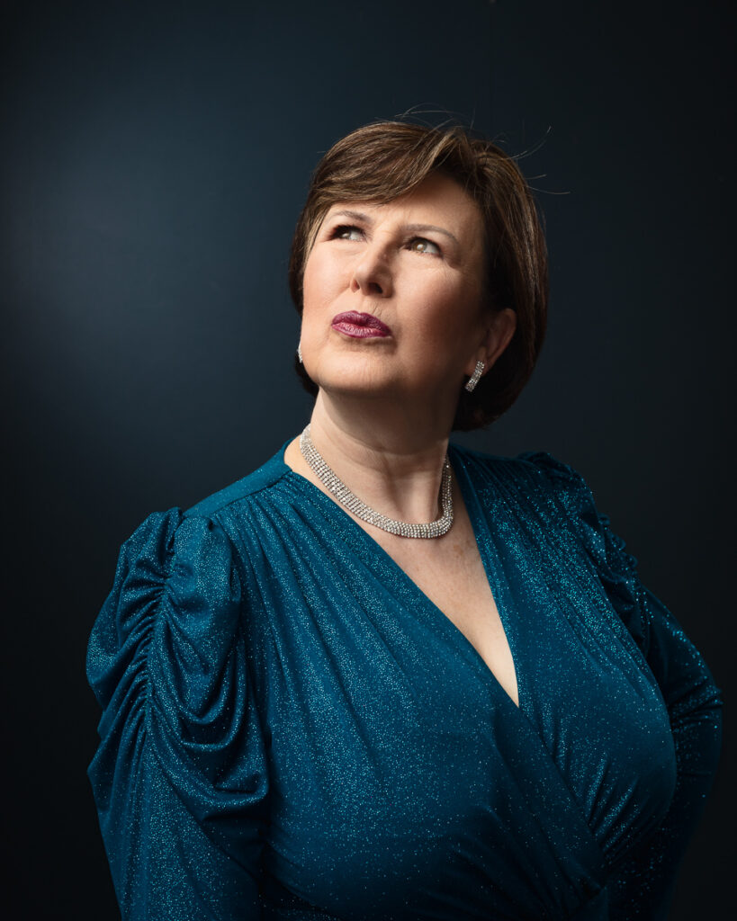 Woman in teal dress looking upwards thoughtfully.