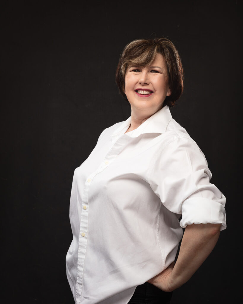 Smiling person in white shirt, dark background.