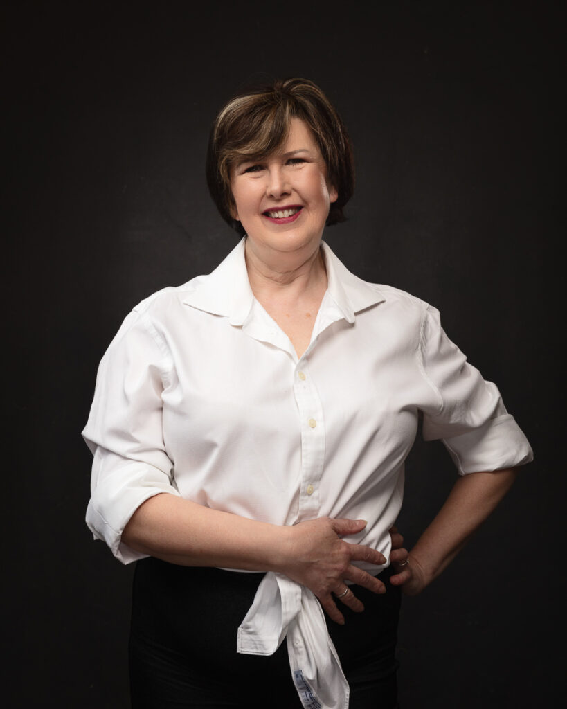 Smiling woman in white shirt against dark background.