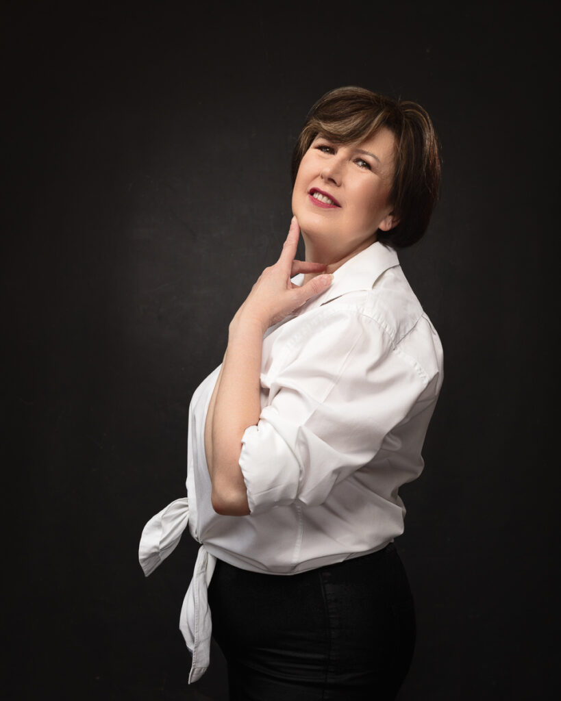 Smiling woman in white blouse against dark background.