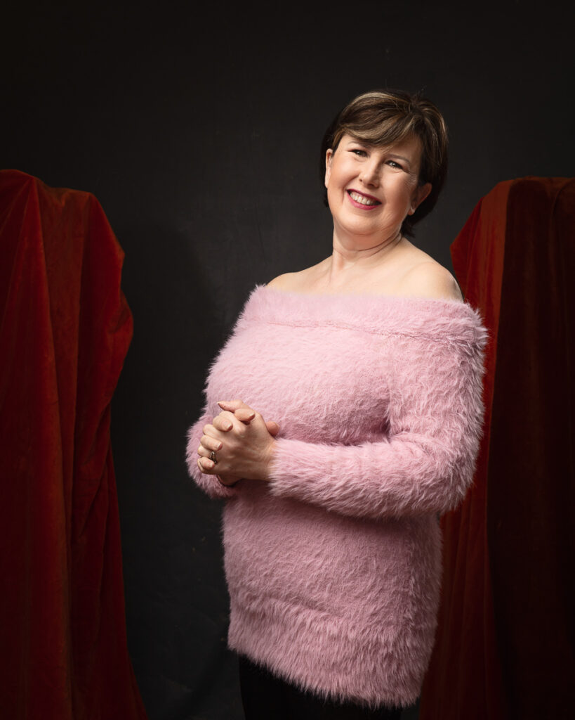 Smiling woman in pink fuzzy sweater, dark background.