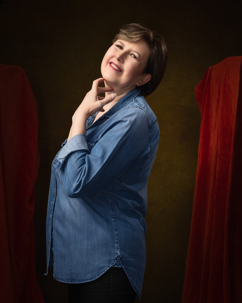 Smiling woman in denim with red curtains backdrop.