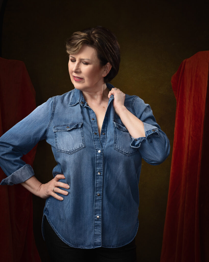 Woman in denim shirt poses thoughtfully.