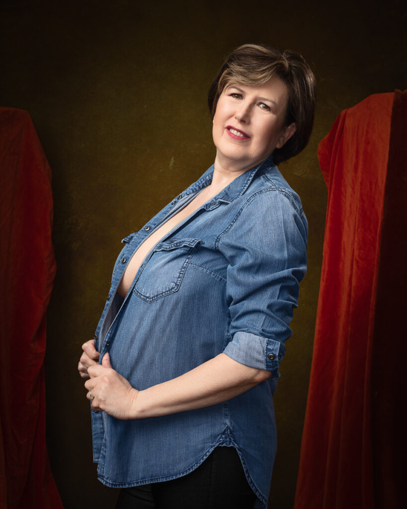 Smiling woman in denim shirt, colourful draped background.