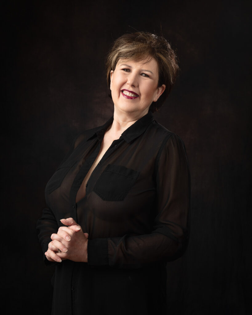 Smiling woman in black shirt with clasped hands.