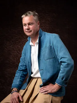 Man in blue jacket posing against dark background.