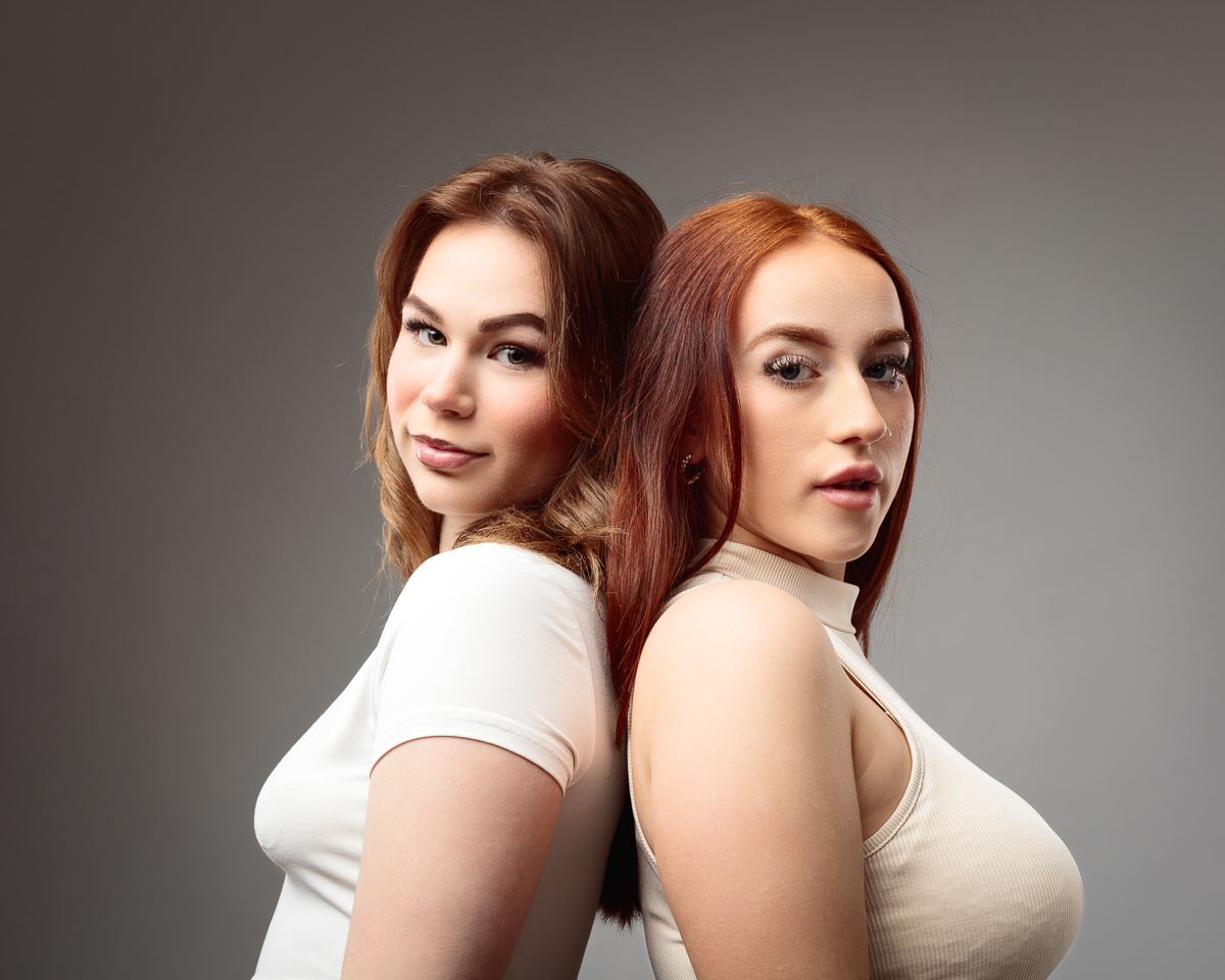Two women back to back, neutral background.