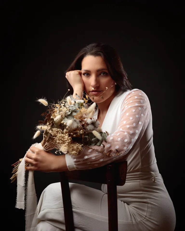 Woman holding dried flower bouquet, wearing white outfit.