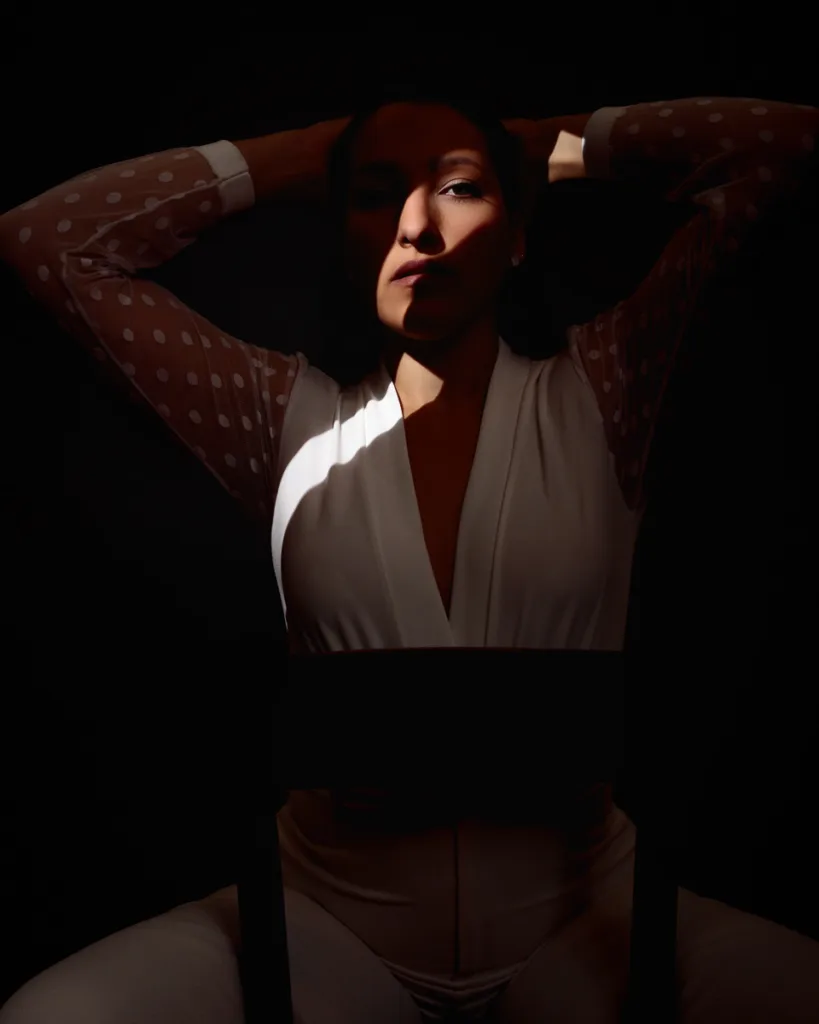 Woman in dramatic shadow, elegant pose with arms raised.