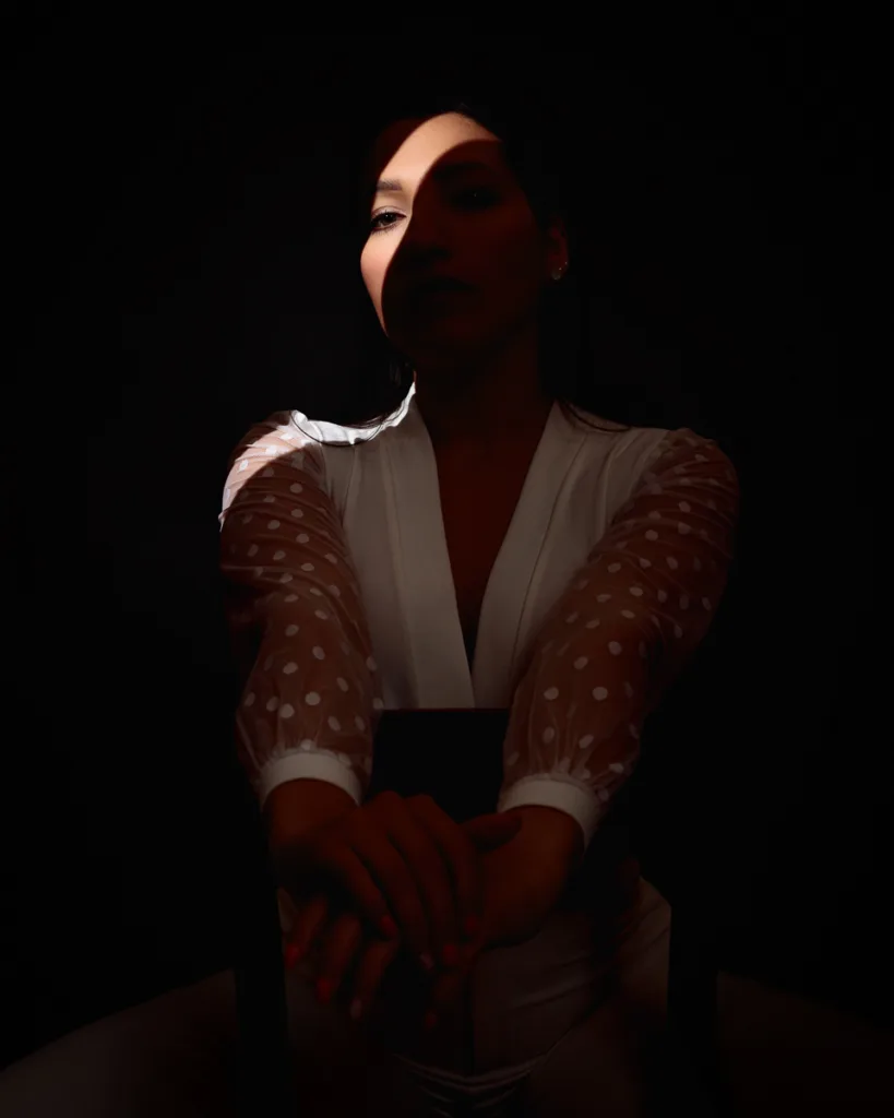 Woman in spotlight, dramatic shadow on face.