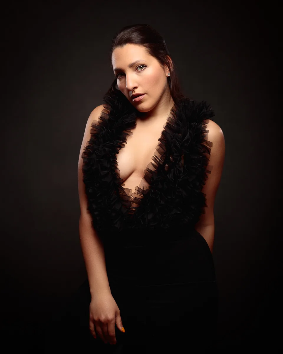 Person posing in elegant black outfit, dark background.