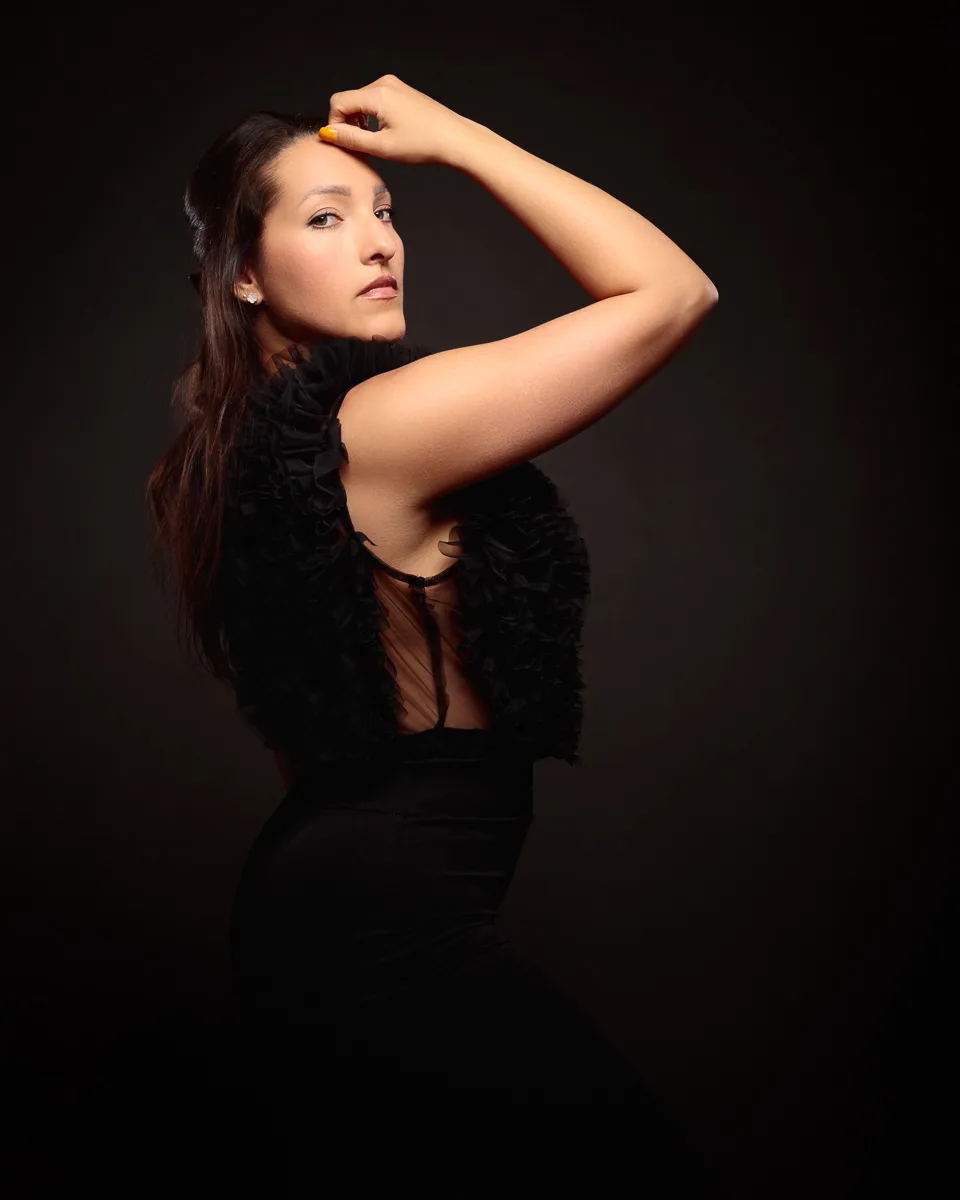Woman posing in elegant black outfit, dark background.