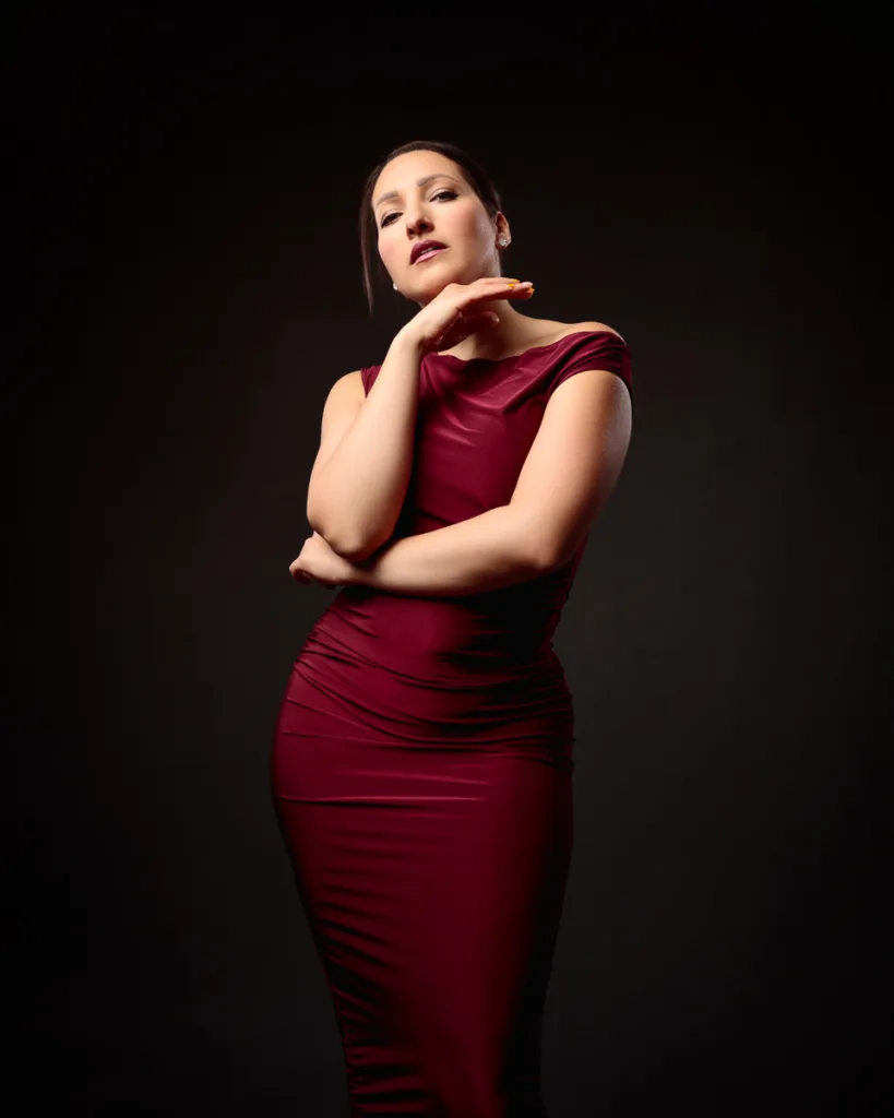 Person poses in elegant burgundy dress against dark background.