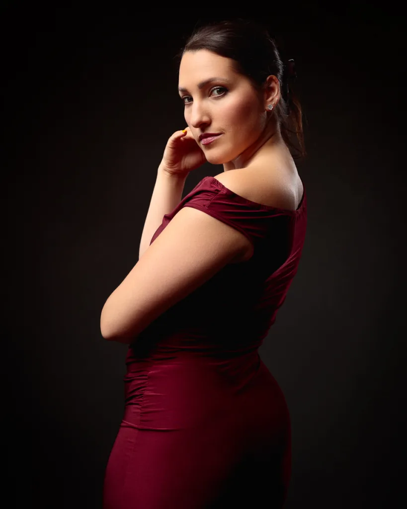 Woman in red dress posing against dark background.