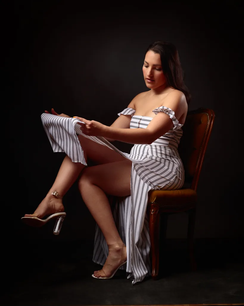 Woman in striped dress sitting elegantly on chair.
