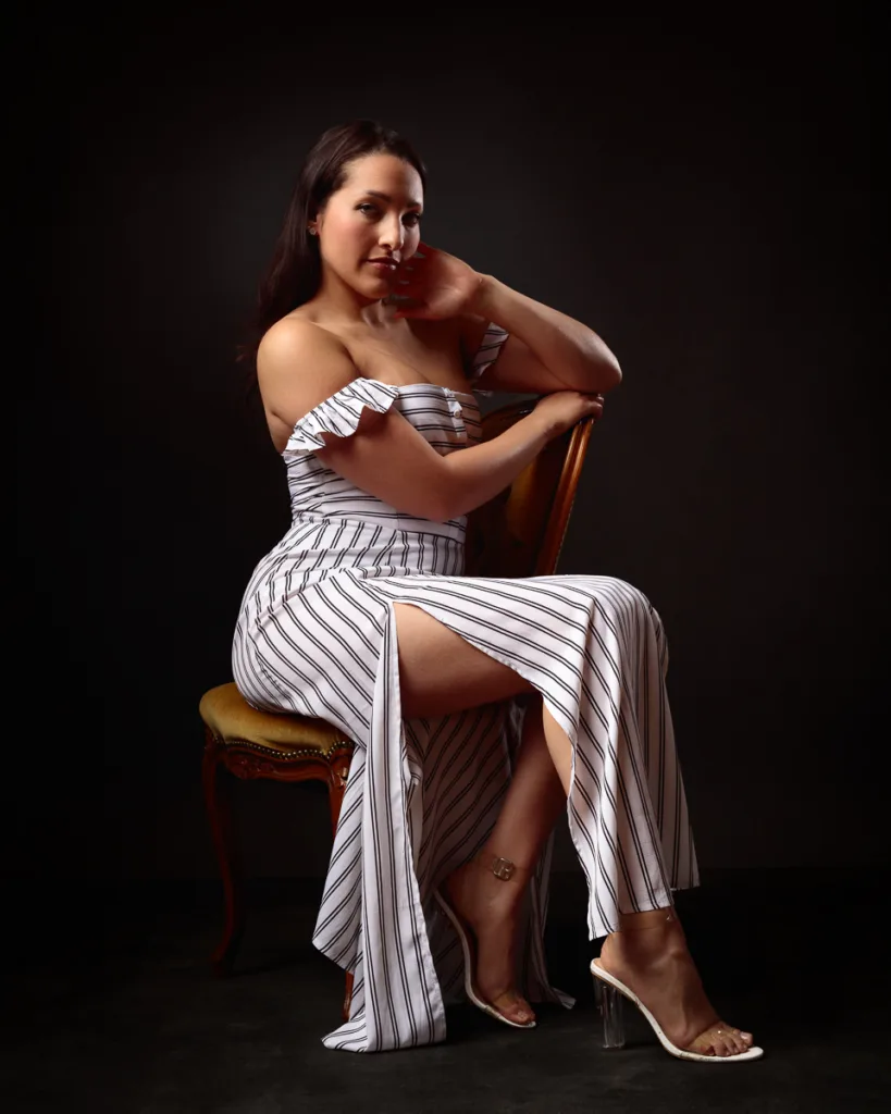 Woman in striped dress seated on chair, elegant pose.