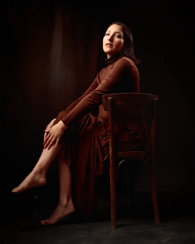 Elegant woman sitting on wooden chair in dark room.