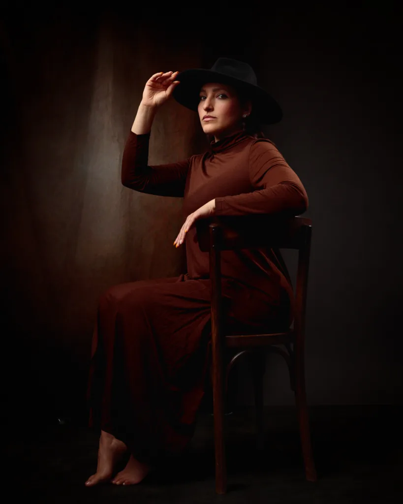 Woman in brown dress and hat, sitting on chair.