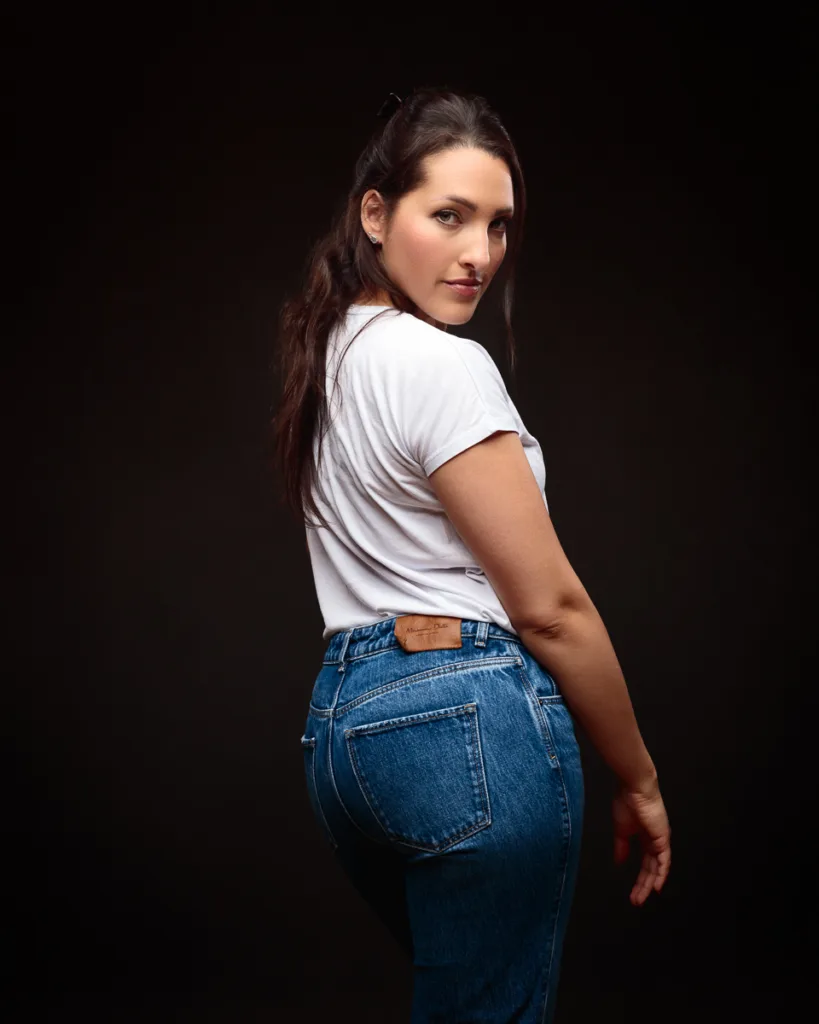 Person posing in jeans with dark background.