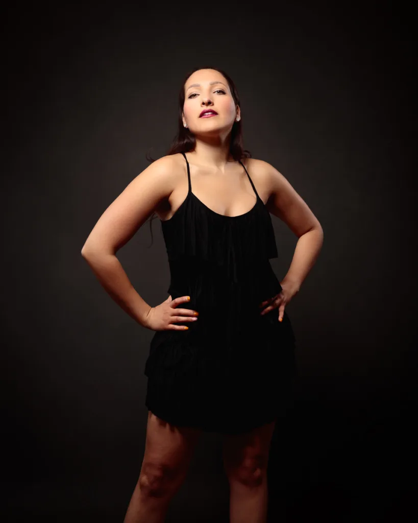 Confident woman posing in black dress, dark background.