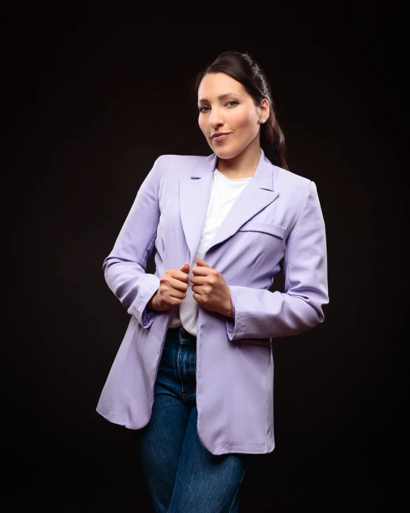 Person in lavender blazer, dark background.